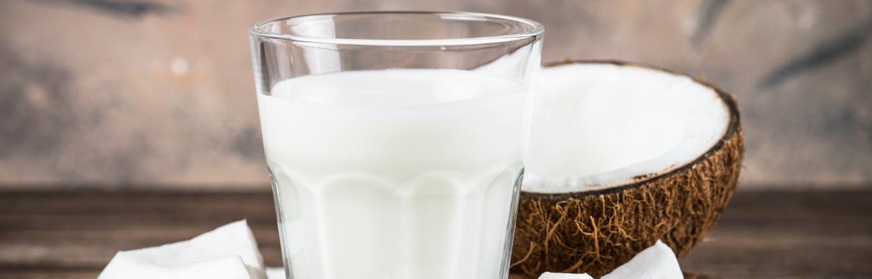 Szklanka mleka ustawiona na blacie z rozłupanym obok kokosem